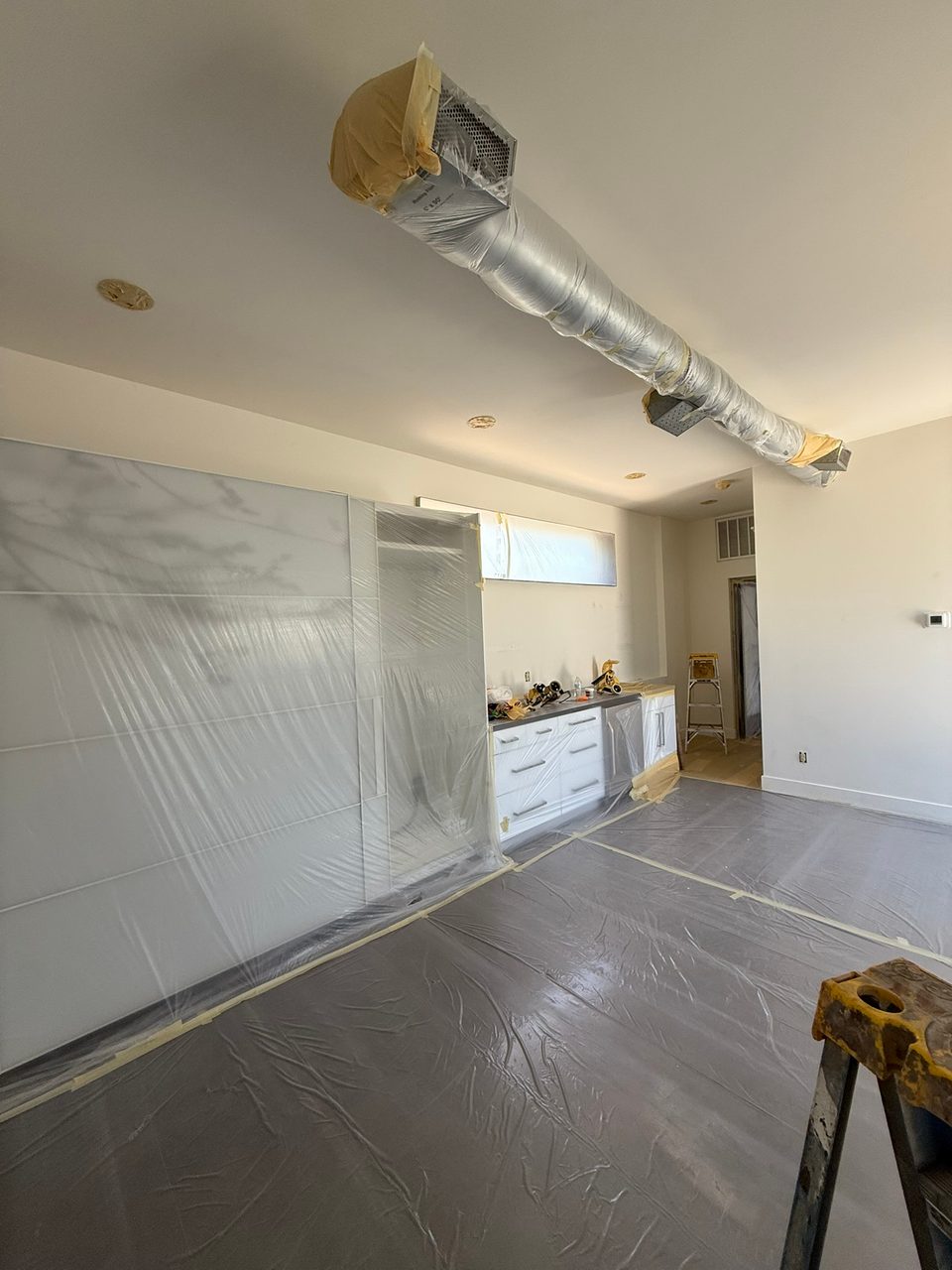 The kitchenette wall during prep, with cabinets and the duct run masked off